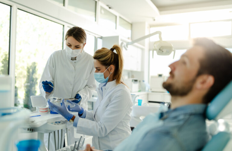 A dentist and an assistant in a dental clinic preparing tools while a patient relaxes in the chair, showcasing professionalism and a commitment to advanced care.